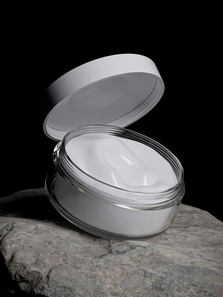 Open jar of white face cream resting on a rock
